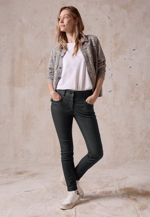 Zwarte skinny jeans met zakdetails, gecombineerd met een grijze gebreide cardigan over een witte T-shirt. Schoenen: witte sneakers.