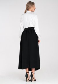 Lange schwarze Rock mit einem taillierten Bund, fließendem Stoff und einer weißen Satinbluse mit langen Ärmeln. Verfügt über einen schwarzen Gürtel und High Heels.