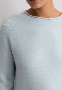 Jasnoniebieski sweter dzianinowy z okrągłym dekoltem i teksturowanym materiałem, przedstawiający zbliżenie na ramiona i okolice klatki piersiowej.