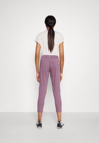 Purple patterned pants with a relaxed fit, featuring a mid-rise waistband and tapered legs. Paired with a light grey short-sleeve shirt.