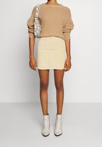 Pull en tricot couleur bronze, mini-jupe en velours côtelé beige clair, et bottines à imprimé serpent gris. Sac à bandoulière avec un motif similaire.