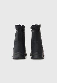 Botas negras hasta el tobillo hechas de un material impermeable, con una suela texturizada, un collar suave y cremalleras laterales para facilitar su uso.