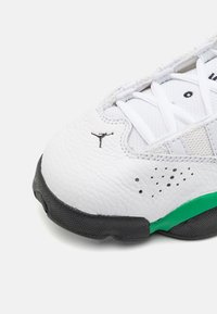 Bílé kožené tenisky s texturovaným povrchem, s černými akcenty, zelenou podrážkou a malým logem na boku. Systém šněrování s síťovými prvky.