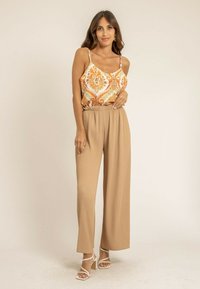 Camisole légère à motifs en orange et crème, associée à un pantalon large beige plissé. Sandales à talons blocs blanches à lanières.