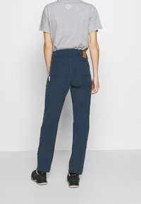 Navy outdoor pants made from durable fabric, featuring a mid-rise waist, back pockets, and reinforced stitching. Paired with a gray t-shirt.