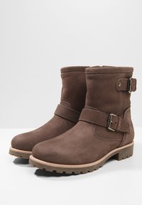 Botas de tobillo de cuero marrón con hebilla lateral, superficie texturizada y suela de goma. Presentan una cremallera para facilitar el uso.
