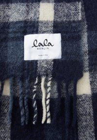 Marine rutete ullsjal med kremfargede detaljer. Har frynsete kanter og en etikett som sier "lala Berlin, laget i Italia." Myk tekstur.