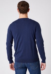 Mörkblå crewneck-tröja i ett mjukt, stickat tyg med långa ärmar och ribbade cuffs, bärs med denimjeans. Inga synliga mönster eller logotyper.