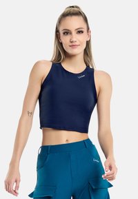 Top corto navy blue in materiale liscio con scollatura rotonda e dettaglio del logo. Pantaloni cargo teal con tasche completano l'outfit.