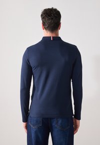 Marine langermet polo skjorte med krage og en liten rød, hvit og blå stripe ved halsen. Myk stoff, slim fit, kombinert med blå jeans.