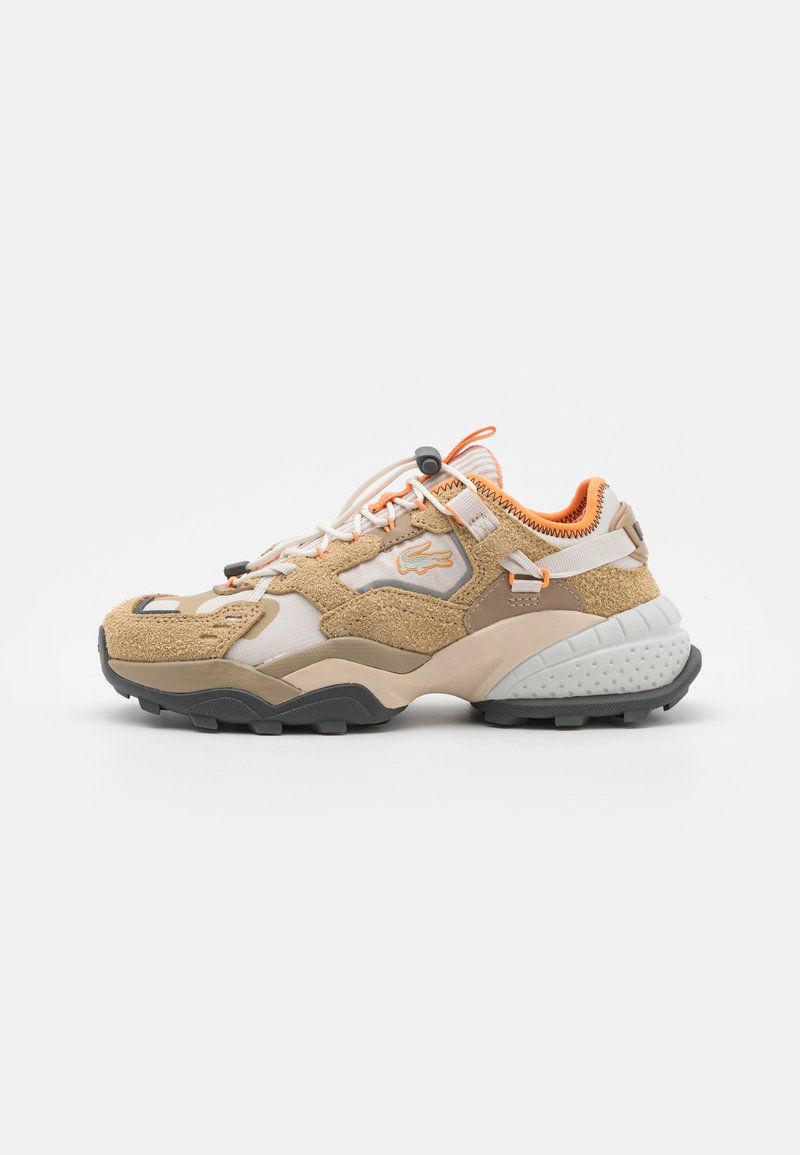 Tan og beige joggesko med en teksturert semsket overdel, oransje detaljer, hvit mesh og en robust svart såle. Har elastiske lisser og sidebranding.