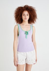 Lilafarge ribbet tanktop med grønne detaljer og en sløyfe ved utringningen, parret med hvite shorts med blomstermønster i utskjæring.