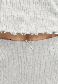Ensemble en maille côtelée gris clair composé d'un haut et d'un bas avec un motif à œillets subtil et un petit nœud décoratif sur la ceinture, laissant le ventre nu apparent.