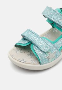 Turkise sandaler med glitrende stropper, utstyrt med borrelås-lukking. Innersålen har et stjernemønster, og yttersålen er i lys farge.