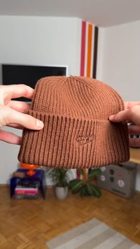 Ruskea ribillinen neulospipo käännetyllä reunuksella, jossa on pieni kirjailtu logo. Materiaali näyttää pehmeältä ja lämpimältä, sopii kylmään säähän.