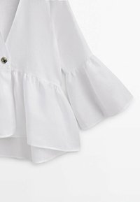 Blouse blanche à manches longues avec patte de boutonnage sur le devant, manches évasées à volants et détail à l'ourlet.