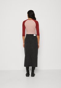 Svetilka z raglan rokavi v svetlo roza in maroon barvi, ujemajoča se s črno jeans maxi krilo, ki ima zadnje žepe in središnjo zarezo. Črne škornje do kolen.
