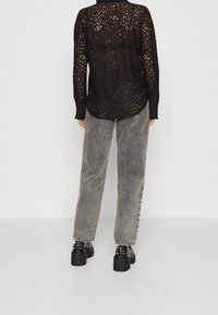 Black lace shirt with long sleeves, open pattern, and buttoned cuffs, paired with gray high-waisted jeans and black platform shoes.
