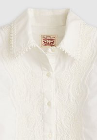 Biela blúzka s jemnými vyšívanými detailmi, s špicatým golierom a zapínaním na gombíky. Viditeľná etiketa Levi Strauss & Co.