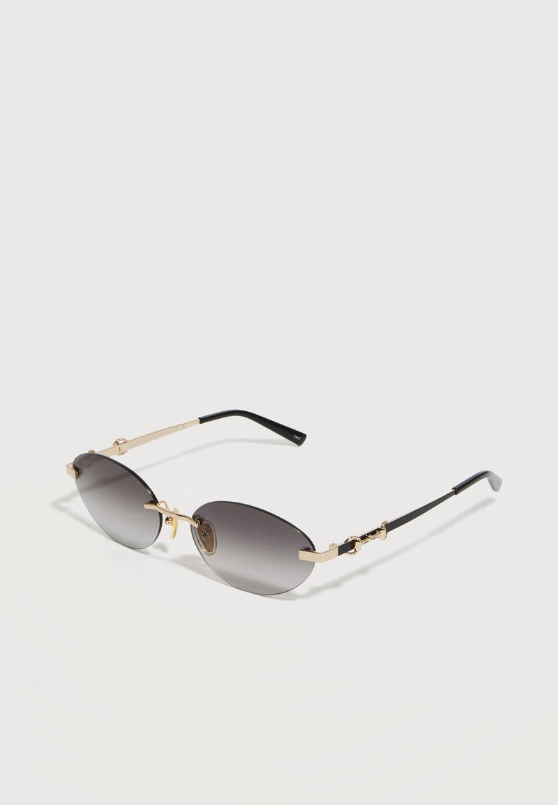 Γυαλιά ηλίου με φακούς γκρι σε σχήμα οβάλ με λεπτά μεταλλικά πλαίσια σε χρυσό και μαύρο και μαύρες άκρες στα κλαδάκια.
