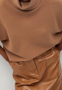 Beige ribbed knit top with a cowl neck paired with brown faux leather high-waisted skirt, featuring structured side pockets and a smooth finish.