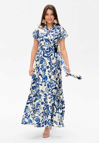 Robe maxi en tissu crème avec des motifs floraux bleus, manches courtes, fermeture à boutons sur le devant et une ceinture en tissu assortie. Texture lisse.