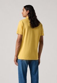 Polo din bumbac galben, cu mânecă scurtă, croi lejer, combinat cu blugi din denim albastru. Prezintă crăpături laterale la tiv.