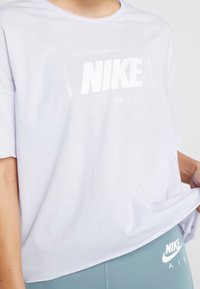 Camiseta blanca de manga corta con gran logo "NIKE" en blanco. Tejido suave, corte relajado, diseño de cuello redondo. Combinada con leggings azul claro que presentan logos.