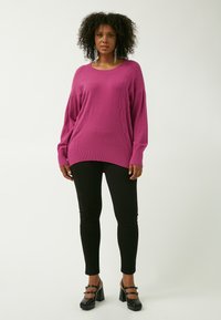 Fuchsia Übergröße Pullover mit geripptem Saum und strukturierten Details, kombiniert mit schwarzen Leggings und klobigen schwarzen High Heels.