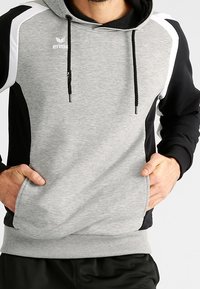 Felpa grigia e nera con accenti bianchi, cordini e tasca a marsupio. Realizzata in un morbido tessuto testurizzato con un design sportivo.