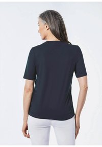 Zwarte short-sleeve t-shirt met een ronde halslijn en een gladde textuur, gedragen met een witte broek, toont de achterzijde en de aansluitende pasvorm.