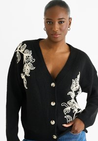 Black knit cardigan with a deep V-neck, featuring white floral embroidery on the left side, and large cream buttons along the front.