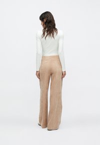 Parte superior ligera de manga larga combinada con pantalones de pana beige de pierna ancha. Los pantalones exhiben un acabado texturizado, con cintura alta y silueta fluida.