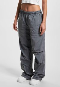 Pantaloni grigi leggeri e larghi con vita elastica e tasche laterali, abbinati a sneaker bianche. Texture liscia.