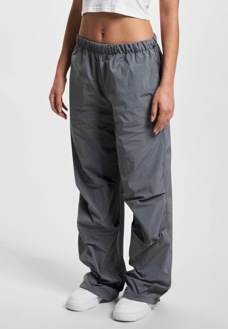 Pantaloni grigi leggeri e larghi con vita elastica e tasche laterali, abbinati a sneaker bianche. Texture liscia.