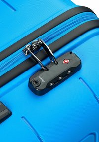 Maleta rígida azul con superficie texturizada, cremallera plateada y candado aprobado por la TSA de color negro con tres diales y un orificio para la llave.