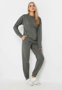 Sudadera gris y pantalones de chándal a juego, hechos de tela suave, con un ajuste relajado y puños acanalados, llevados con zapatillas blancas.