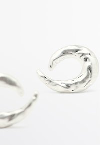 Zilveren oorbellen met een gedraaide halve maansvorm, voorzien van een gestructureerd oppervlak en een gepolijste afwerking. Twee zichtbare exemplaren op de afbeelding.