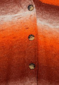 Sweter z dzianiny w gradientowych odcieniach pomarańczy o miękkiej fakturze, z dużymi, okrągłymi brązowymi guzikami na przodzie.