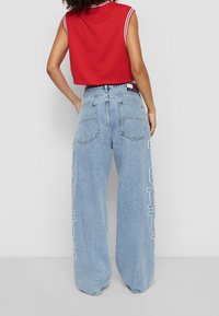 Červený zkrácený top bez rukávů s bílými pruhy u límce, spárovaný se světle modrými širokými džíny s bílým nápisem na boku.