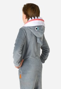 Grijze haai-thema romper met een pluizige textuur, voorzien van een capuchon met vinnen, ogen en een gestreepte kraag. Inclusief een zijzak met een oranje label.