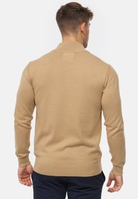 Pull beige en maille avec un ourlet et un col côtelés, fabriqué en un matériau tricoté doux. Il présente des manches longues et une coupe ajustée.