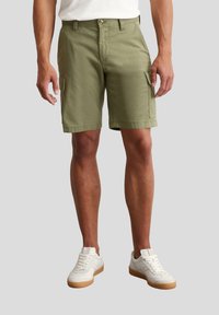 Khaki Cargo-Shorts aus Baumwolle, mit zwei Seitentaschen, geradem Schnitt und sauberem Saum. Kombiniert mit weißen Sneakers.