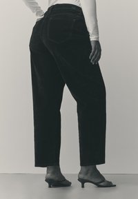 Sorte kordfløjlsbukser med høj talje og lige ben. Bagpå er der to lommer og diskret syning. Kombineret med sorte sandaler med hæl.