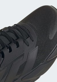 Black athletic shoe with a textured upper, featuring laces and a molded rubber sole. Design includes prominent branding on the side.