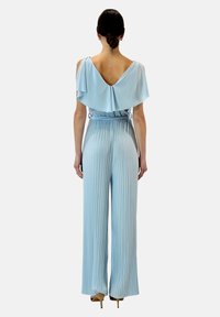 Ljusblå jumpsuit med en vid överdel och vertikala veck, med V-ryg och elastisk midja. Slät textur, vida ben.