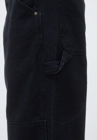 Σκούρο τζιν παντελόνι με ίσια γραμμή, πλαϊνές τσέπες και μια μικρή λεπτομέρεια κουμπιού. Η υφή εί�ναι λεία με ελαφρές φθορές.