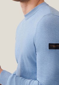 Maglione crewneck azzurro chiaro realizzato in materiale morbido, con polsini a coste e un'etichetta nera sulla manica con la scritta "CAVALLARO NAPOLI".