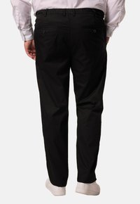 Zwarte relaxed-fit broek met een drawstring tailleband en twee achterzakken, gemaakt van gladde stof; gedragen met witte sneakers.