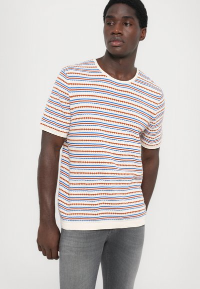 T-shirt κοντομάνικη με κόκκινες, μπλε και άσπρες οριζόντιες ρίγες; στρογγυλή λαιμόκοψη; υφασμάτινη υφή; συνδυασμένη με γκρι τζιν.